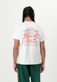 Biele bavlnené tričko so skôr farebn�ým grafickým dizajnom na chrbte, vrátane textu "JACKER STREET FOOD" a ilustrácie hot dogu.