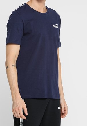 Camiseta de algodón de color azul marino con mangas cortas, escote redondo y logo blanco en el pecho. Presenta una marca en contraste a lo largo de los hombros.