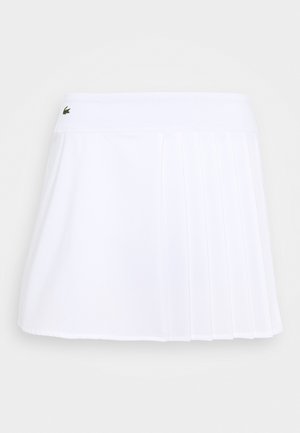 Bílá plisovaná sukně s šortkami vyrobená z lehké tkaniny, s páskem zdobeným logem. Design je krátký a sportovní, vhodný pro aktivní nošení.