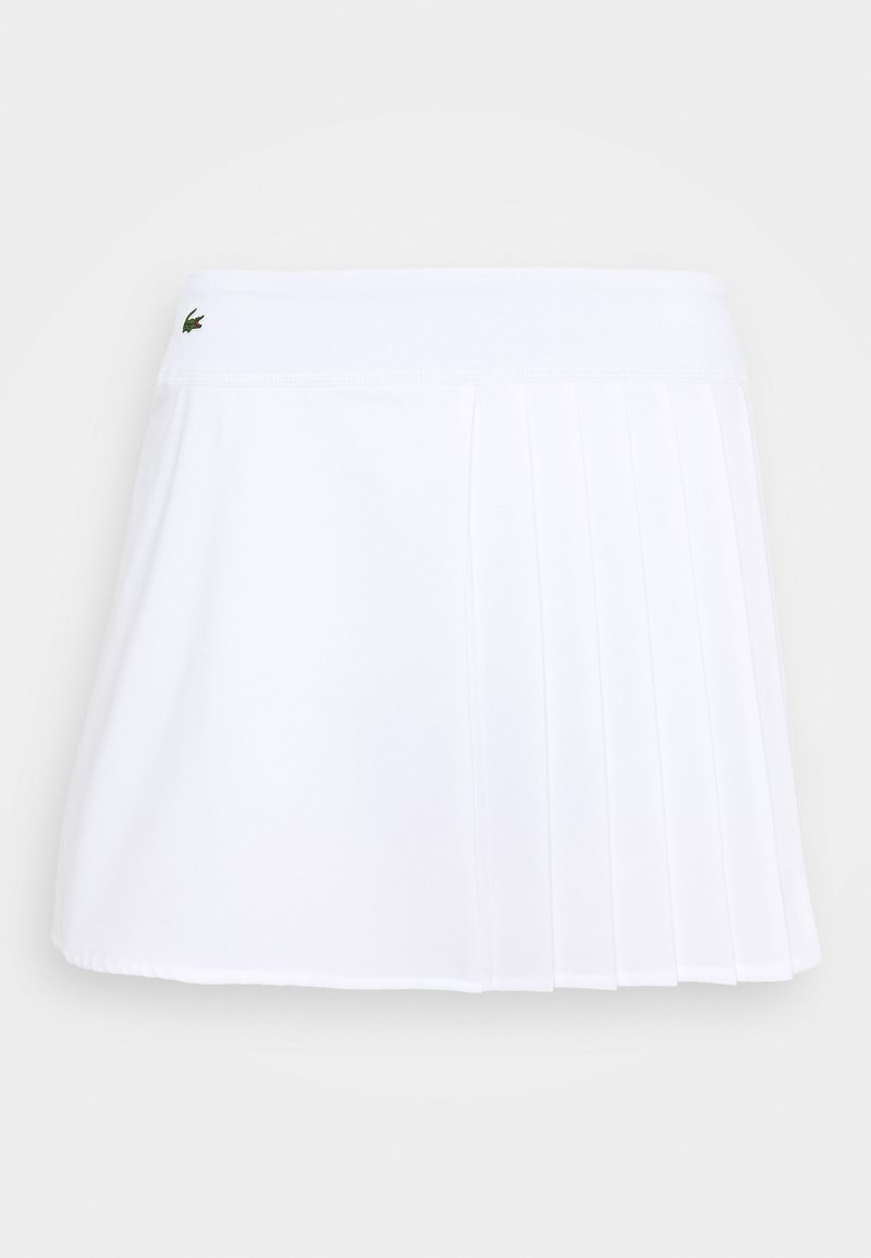 Bílá plisovaná sukně s šortkami vyrobená z lehké tkaniny, s páskem zdobeným logem. Design je krátký a sportovní, vhodný pro aktivní nošení.