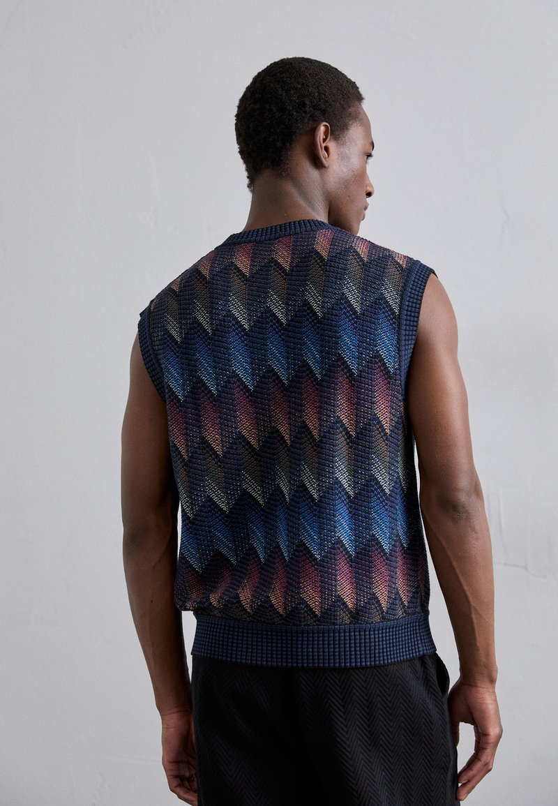 Gilet senza maniche lavorato a maglia con un motivo geometrico nelle tonalità di blu, rosso e crema. Tessuto testurizzato con scollo e orlo a coste.