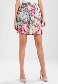 Jupe fleurie avec un fond rose, ornée de feuilles vertes et de fleurs rouges. Taille élastique et tissu léger. L'ourlet atteint le milieu des cuisses.