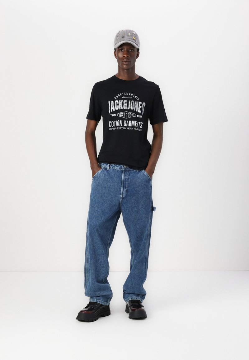 Black T-shirt with white text, loose blue denim jeans, and black chunky shoes. Gray cap with metallic details. Simple, casual outfit.