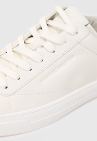 Valge nahast tenniseking, ümmarguse toe, tekstuurse ülemise osa, tasaste paelte ja printitud "TOMMY HILFIGER" logoga küljel. Kummerk, minimaalne disain.