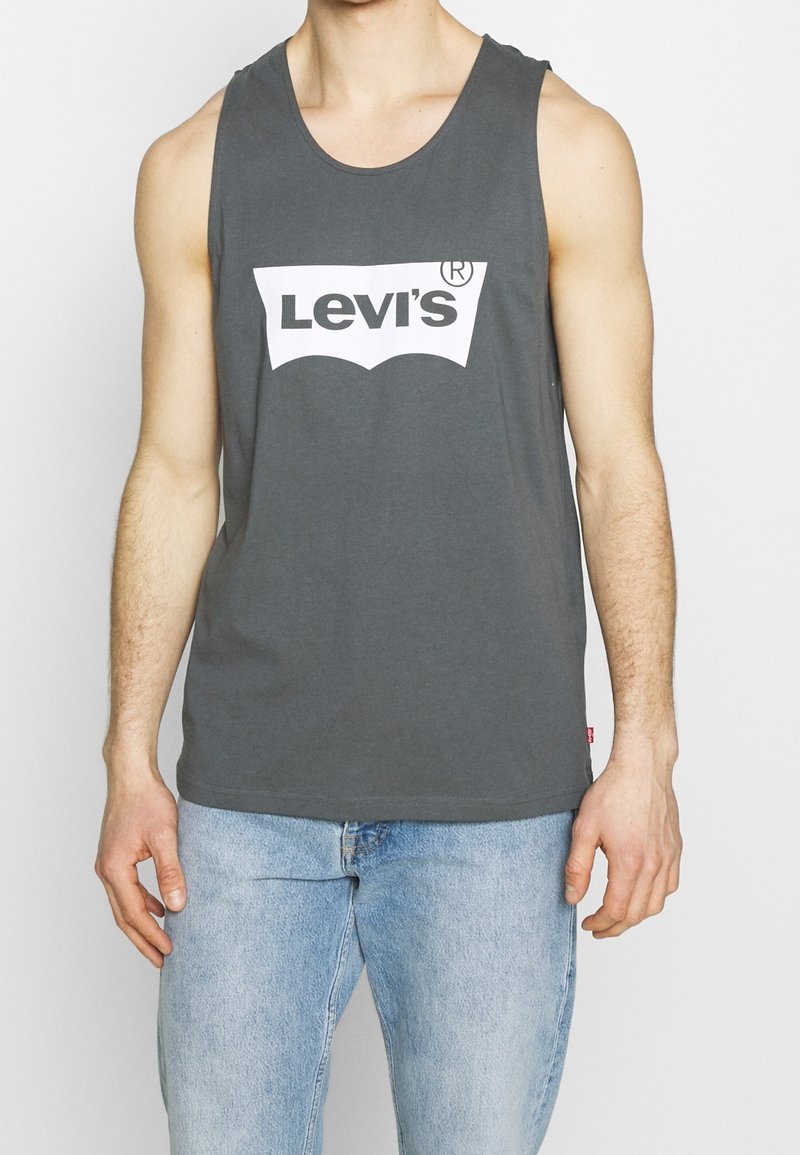 Grå bomullströja utan ärmar med en vit Levi's-logotyp. Rundad halsringning och ärmlös design, kombinerad med ljusblå denimjeans.