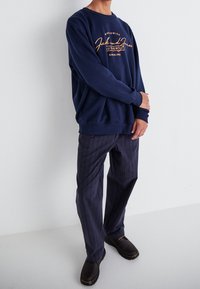 Sweat-shirt bleu marine avec un texte graphique orange ; poignets et ourlet côtelés. Associé à un pantalon à rayures noires et des chaussures noires.
