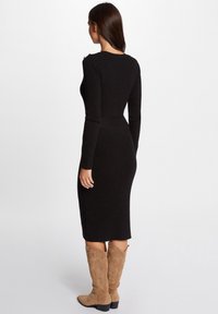 Abito nero a coste con maniche lunghe, silhouette aderente e vita texturizzata. Abbinato a stivali in suede beige al ginocchio con cuciture decorative.
