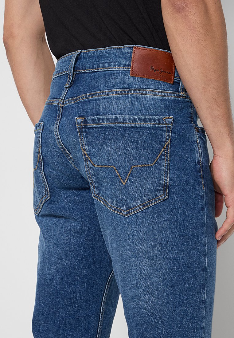 Verwaschene blaue Jeans aus Denim mit hohem Bund, auffälligen Gesäßtaschen mit v-förmiger Naht und einem braunen Leder-Brandpatch.
