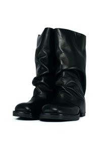 Un paio di stivali neri in pelle fino al polpaccio con suole piatte e un design leggermente sfilato, esposti su uno sfondo bianco.
