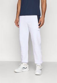 Białe sportowe spodnie o slim fit z bocznymi akcentami z siateczki, w połączeniu z białymi sneakersami z czarnym logo i teksturowaną podeszwą.