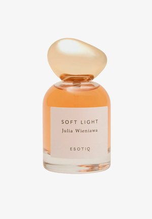 Przezroczysta szklana butelka na perfumy z zaokrągloną bursztynową nakrętką. Zawiera jasno pomarańczowy płyn. Etykieta z napisem „SOFT LIGHT” oraz „Julia Wieniawa.”