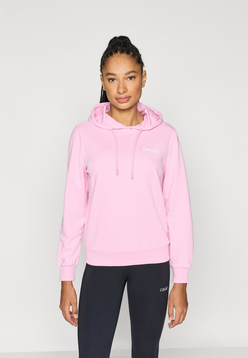 Pink hoodie with long sleeves, drawstring hood, and ribbed cuffs; features "LIMITLESS" text in white on the chest; paired with black leggings.