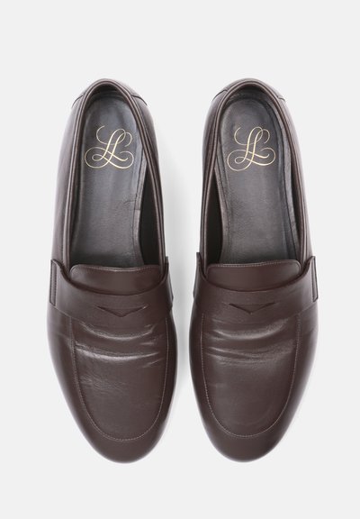 Paire de mocassins en cuir marron foncé, sans lacets, avec des coutures subtiles et des initiales décoratives dorées à l'intérieur de chaque chaussure.