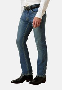 Jeans de mezclilla azul con un ajuste slim, costuras en contraste y cintura de altura media, combinados con botas de vaquero negras.