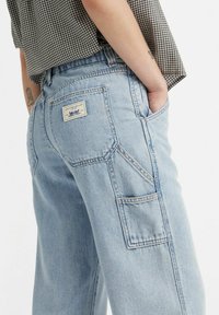 Pantaloni cargo in denim blu chiaro caratterizzati da una vestibilità relaxed, tasche posteriori e un'etichetta con il marchio sulla vita. Texture morbida con un design classico.