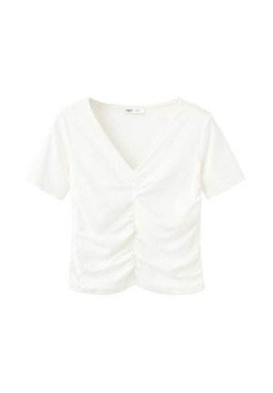 Jonge vrouw die een gerimpeld wit crop top en donker wijde broek met knopdetails draagt, een grijze schoudertas bij zich heeft en staat tegen een effen achtergrond.
