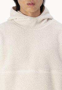 Felpa con cappuccio in bianco sporco con superficie texture, colletto alto e dettagli delle cuciture in evidenza. Design leggero e informale.