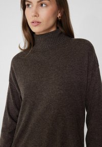 Suéter marrón de cuello alto con costillas y mangas largas, elaborado en un tejido suave y texturizado. Presenta un corte holgado para mayor comodidad.