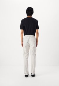 Weiße Cargo-Hose mit elastischem Bund und zwei seitlichen Cargo-Taschen, kombiniert mit einem schwarzen T-Shirt mit kurzen Ärmeln und schwarzen Turnschuhen.