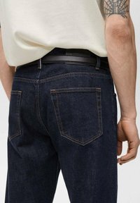 Mørkeblå denim jeans med en tætsiddende pasform, der har brune sømme, to baglommer og et sort bælte med en glat overflade.