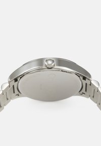 Rustfritt stål klokke med rund urskive og en polert sølvfinish. Har en strukturert krone og et metall lenke armbånd.