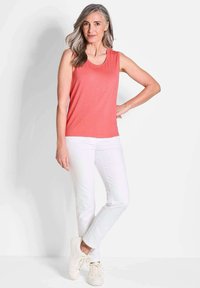 Korallenfarbener ärmelloser Top, kombiniert mit weißen, geraden Hosen und hellen Sneakers. Glatter Stoff und lockere Passform. Minimalistisches Design und klare Linien.