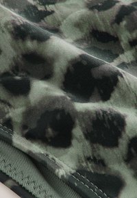 Gros plan d’un tissu vert avec un motif camouflage foncé et des coutures visibles le long du bord.