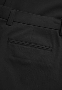 Fekete nadrág, sima anyagból, egyenes elülső résszel és egyetlen hátsó zsebbel, finom varrási részlettel.