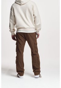Krémová mikina s kapucí a volnějším střihem, doplněná hnědými cargo kalhotami s bočními kapsami. Celý outfit doplňují bílé tenisky.