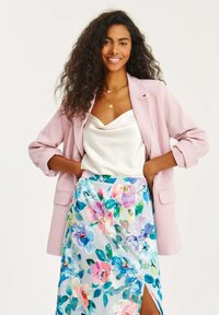 Světle růžový blejzr přes bílý saténový top, doplněný květinovou sukní v pastelových barvách. Sukně má boční rozparek.