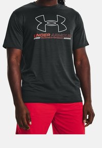 Czarny sportowy t-shirt z krótkim rękawem z szarym logo Under Armour i czerwonym napisem, wykonany z teksturowanego, oddychającego materiału.