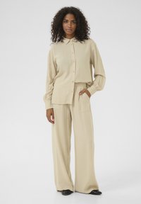 Chemise beige à col et à manches longues, associée à un pantalon beige à jambes larges avec une taille élastique et des poches.