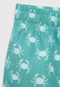 Turfärgad badshorts med elastisk midja, med ett upprepat mönster av vita krabbor. Materialet är slätt med en lätt glansig yta.