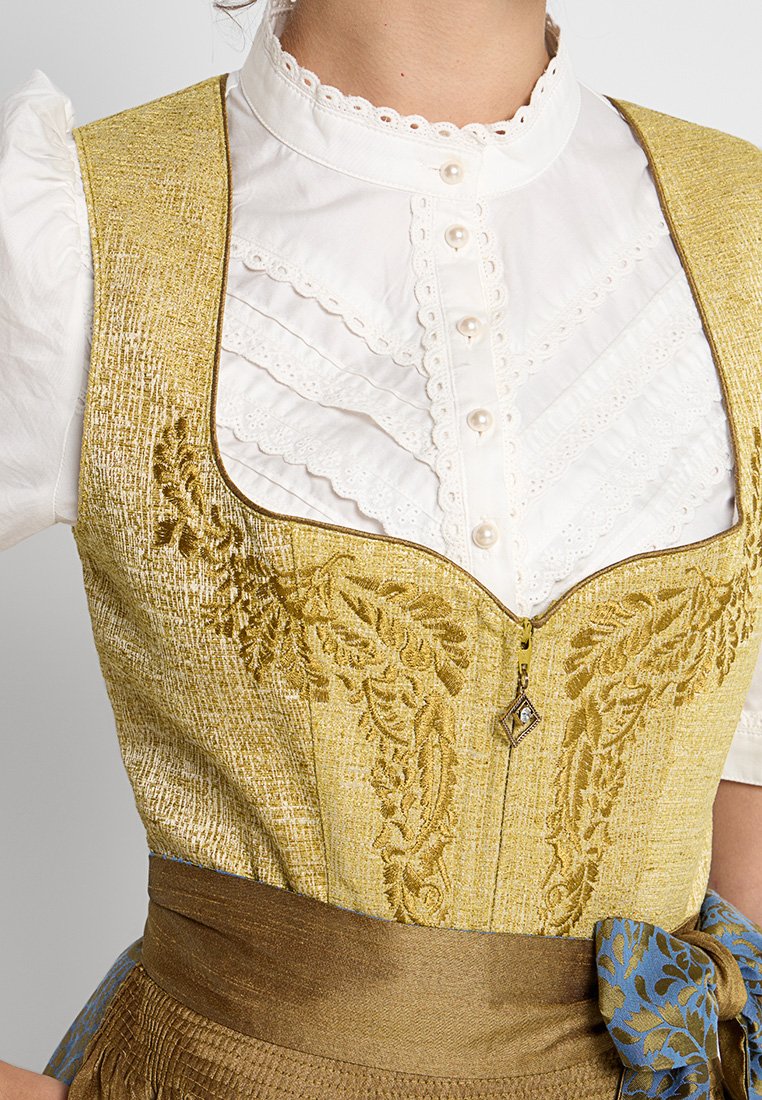 Gelb und gold gestickter Mieder über einem weißen, gerafften Hemd, mit einem Reißverschluss vorne und braunem Gürtel mit blauen Blumenakzenten.