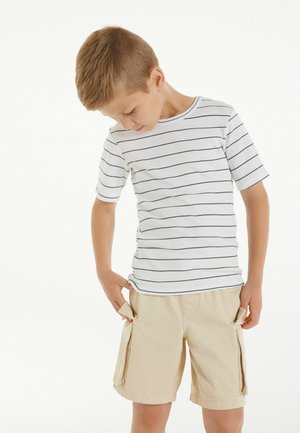 Weißes kurzärmliges gestreiftes Hemd mit schwarzen Linien, kombiniert mit beigen Cargo-Shorts mit seitlichen Taschen. Einfaches, lässiges Outfit für Kinder.