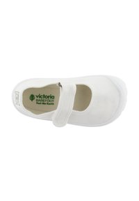 Zapato tipo Mary Jane de lona blanca con una correa de Velcro, interior texturizado y suela de goma ligera. Logo visible en el interior.