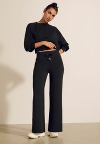 Felpa nera in cotone con maniche ampie abbinata a pantaloni della tuta neri, dotati di vita con cordino, vestibilità comoda e tessuto testurizzato.