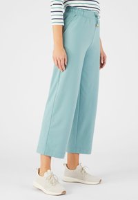 Licht teal kleurige wijde broek van een zachte stof, met een elastische tailleband en trekkoorddetail, gecombineerd met lichtgekleurde gebreide sneakers.