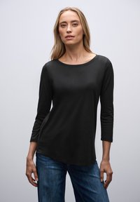 Czarny longsleeve z okrągłym dekoltem, miękka tekstura i luźny krój. Połączony z niebieskimi dżinsami w casualowym stylu.