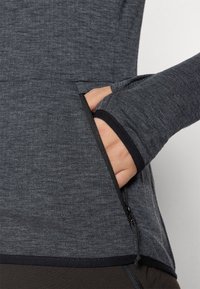Maglietta grigia a maniche lunghe con tasca con zip e fori per il pollice, realizzata in un morbido tessuto testurizzato e con un design aderente. Accenti neri.