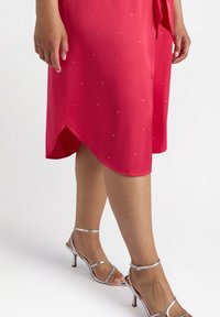 Rotes Kleid mit einer glatten Textur, verziert mit kleinen funkelnden Applikationen, asymmetrischem Saum, kombiniert mit silbernen, Riemchen-Absätzen.