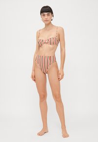 Svītraini bikini komplekts ar bandeau stila topu ar loku detaļu un augsto jostasvietu apakšējām daļām, sarkanā un krēmkrāsā ar gludu auduma tekstūru.