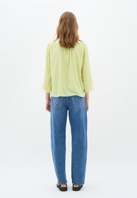Blusa verde chiaro con maniche a sbuffo e jeans blu a vita alta con una vestibilità comoda e tasche posteriori. Tessuto liscio, stile informale.