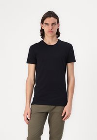 T-shirt noir à col ras du cou en coton lisse, doté de manches courtes et d'une coupe ajustée. Un petit logo est situé sur l'épaule droite.