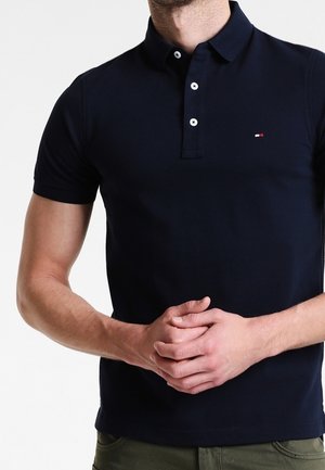 Polo bleu marine avec une texture douce, manches courtes, patte à deux boutons, et un petit logo brodé sur la poitrine.