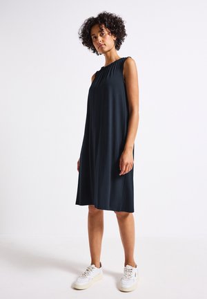 Sleeveless, dark blue dress with gathered neckline, knee-length hem, and smooth fabric. Model wears white sneakers. Simple A-line design.