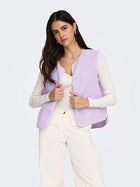 Chaleco sin mangas color lavanda claro con tejido texturizado y cierre de presión, superpuesto sobre una camiseta blanca de manga larga, combinado con pantalones blancos.