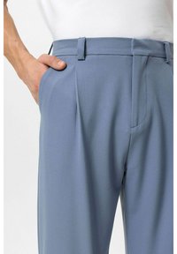 Lichtblauwe geplooide broek met zijzakken, gladde textuur, getailleerde pasvorm en riemlussen. De tailleband heeft een subtiel ontwerp.