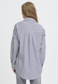 Striped long-sleeve shirt in blue and white cotton, featuring a pointed collar, buttoned cuffs, and a curved hemline. Relaxed fit.