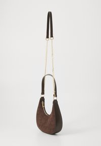 Sac à main en cuir suédé marron avec une forme courbée. Équipé d'une courte bandoulière en cuir et d'un accent en chaîne dorée. Fermeture éclair sur le côté.